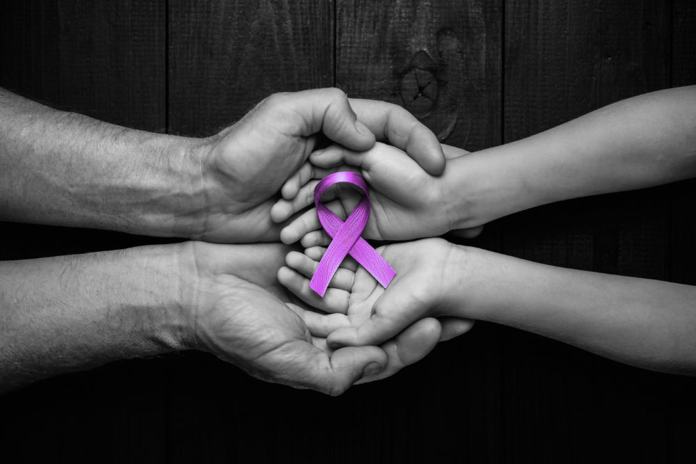 CBD Oil and Epilepsy concept with hands holding purple ribbon’s top view on black wooden background.