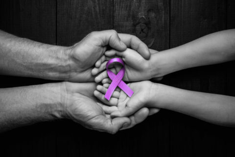 CBD Oil and Epilepsy concept with hands holding purple ribbon’s top view on black wooden background.